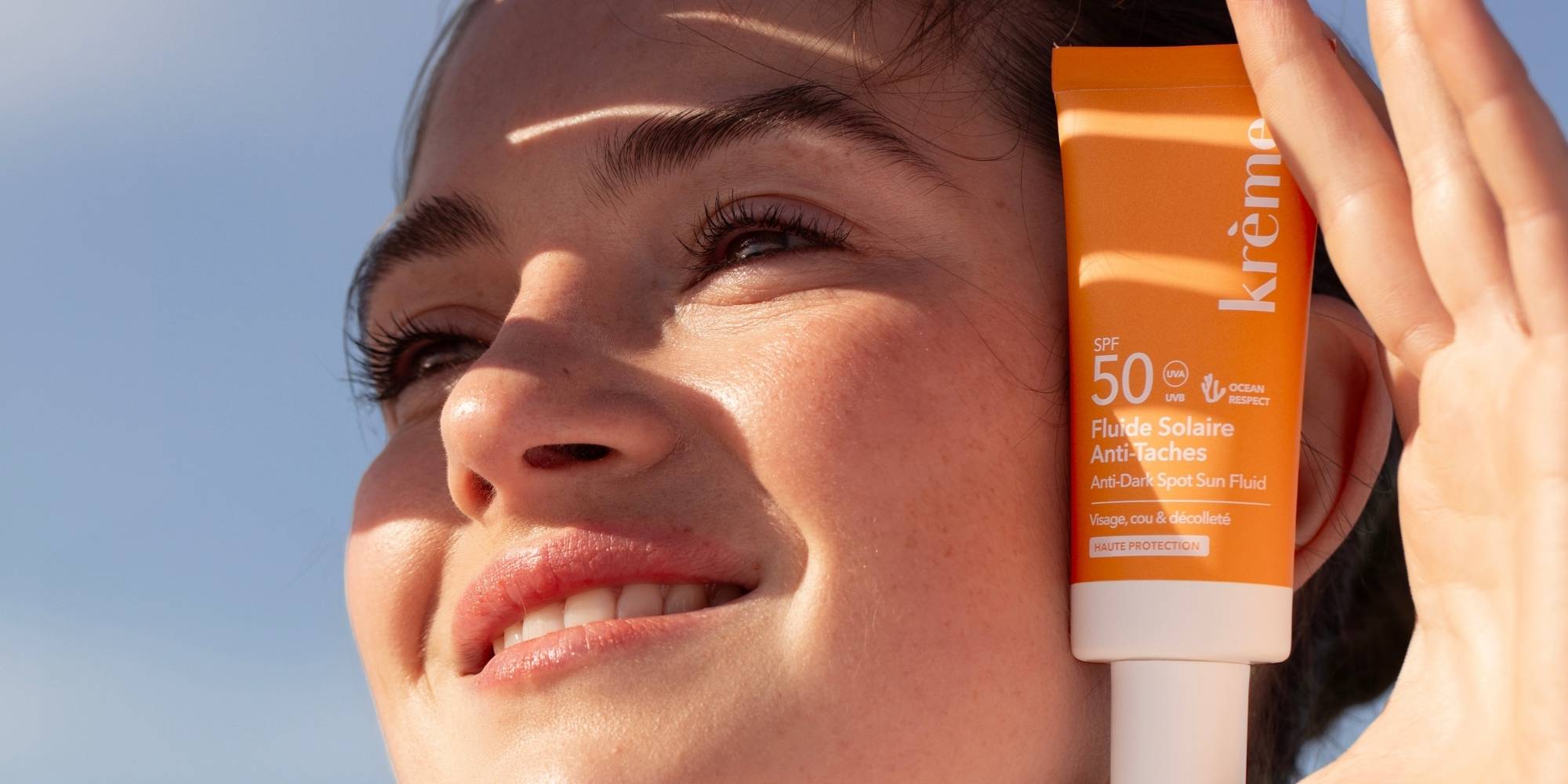 Femme sous le soleil qui montre sa crème solaire anti-taches